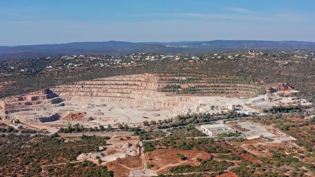 Vast industrial landscape showing an open pit mine with stepped terraces for extracting stone and aggregate. Highlighting the significant environmental impact of the excavation on the natural terrain