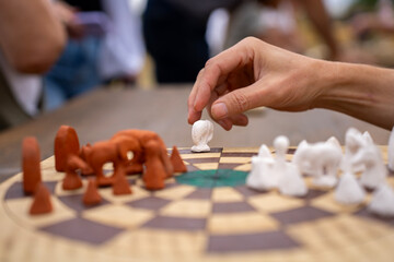 A hand moves a white chess piece on a chessboard opposite brown pieces, with other white pieces nearby. © Marina
