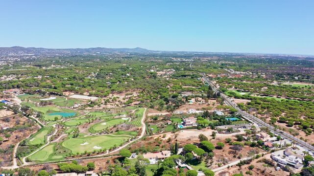 Expansive aerial view showcasing the lush green golf courses and exclusive residential properties of vale de lobo in algarve, portugal, under a clear blue sky on a sunny summer day