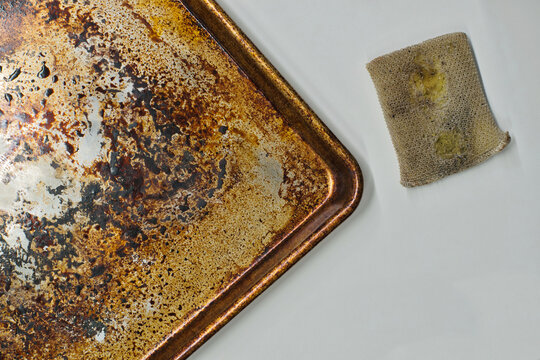 Dirty stained cookie sheet aluminum baking pan bakeware with old cleaning sponge.