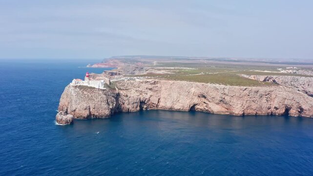Majestic aerial view of the iconic cape st. Vincent lighthouse perched atop dramatic cliffs overlooking the vast blue atlantic ocean on a sunny day in the algarve region of portugal