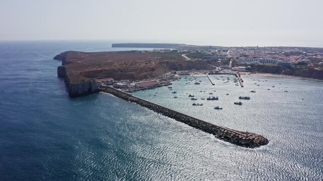 Beautiful aerial perspective of the picturesque fishing port of baleeira and the town of sagres, showcasing the rugged algarve coastline, long stone breakwater, and boats in the harbor