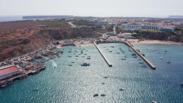 Beautiful aerial view showing the bustling fishing port of sagres with many boats in the harbor, the adjacent baleeira beach, and the scenic algarve coastline on a sunny summer day in portugal