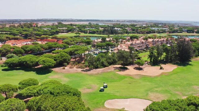 Aerial view of a stunning golf course in vale de lobo, portugal, with electric carts driving on the green fairway next to luxury villas and pine trees in the exclusive quinta do lago resort