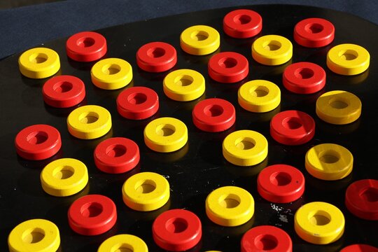 Petites pi&egrave;ces de bois circulaires de couleur jaune et rouge pos&eacute;es sur une surface noire. Jeu compos&eacute; d'&eacute;l&eacute;ments plats et ronds pouvant &ecirc;tre d&eacute;plac&eacute;s.