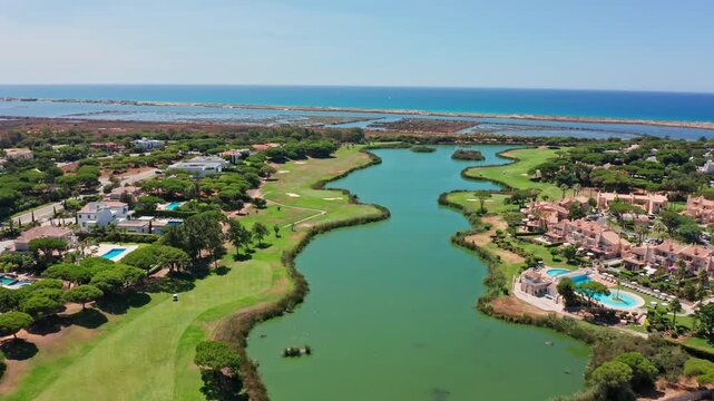 Sunny aerial view flying over the beautiful green vale do lobo golf course with its lake and luxury villas, overlooking the stunning atlantic ocean coastline in the algarve region, portugal