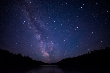 Fototapeta premium Milky Way Reflected Over Calm Lake and Forest at Night
