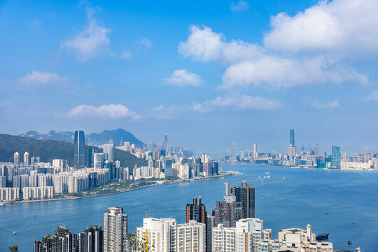 Expansive view across Victoria Harbour with the skylines of Hong Kong Island and Kowloon visible on both sides under a clear blue sky.