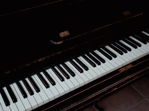 Old upright piano with black and white keys, dark wooden body and visible wear. Vintage musical instrument for music, culture, education, creativity, nostalgia and restoration concepts.