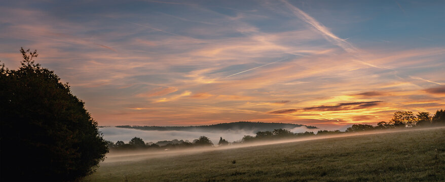 Starker Sonnenaufgang mit viel dichtem Boden Nebel &uuml;ber den Felder und H&auml;usern, Wald in der Ferne