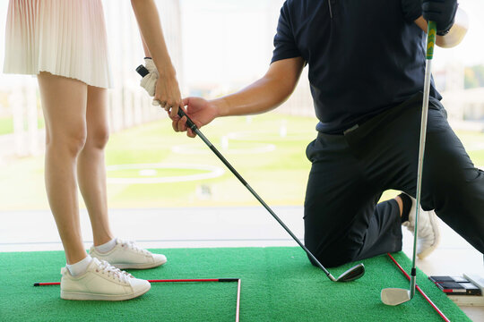 Golf instructor teaching young woman stance at driving range