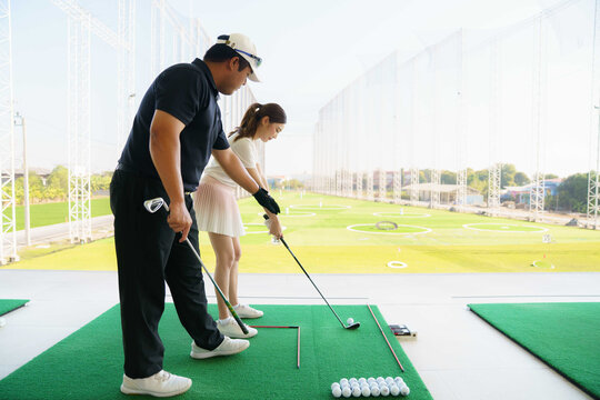 Golf instructor teaching young woman stance at driving range