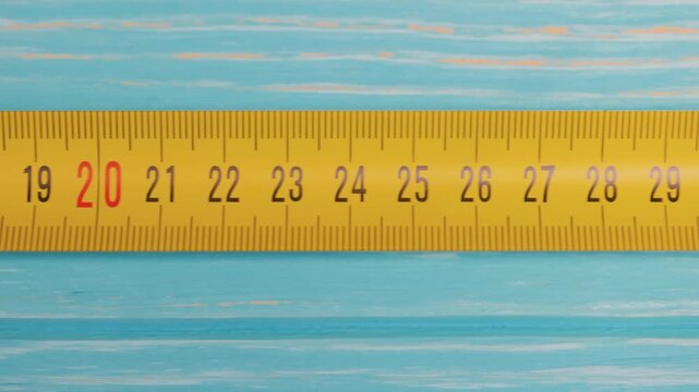 Yellow measuring tape tool sliding across blue wooden surface in motion.