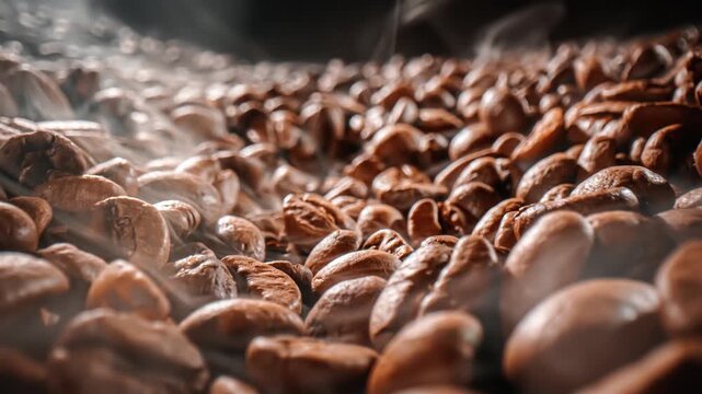Close up video of aromatic coffee beans roasting process with smoke and steam, generating rich brown color and fragrant aroma.