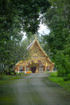 Beautiful Lanna style Buddhist temple surrounded by green trees with path road at Wat Phuket in Pua district, Nan province, Thailand.