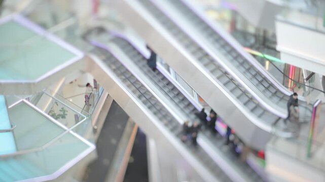 People moving on escalators inside modern shopping mall with dynamic lighting effects.