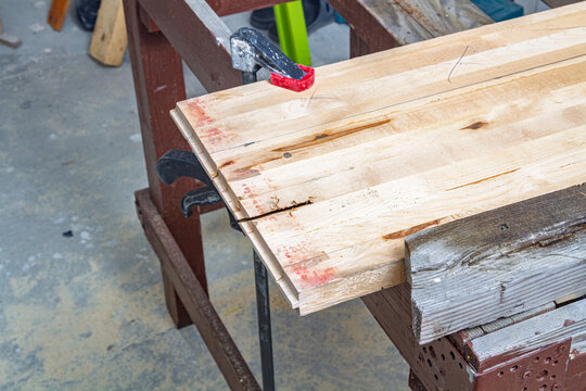 Wooden parquet boards secured with clamps on a workbench for carpentry. Lumber preparation for woodworking and construction. DIY workshop project. Building materials, repair and furniture making