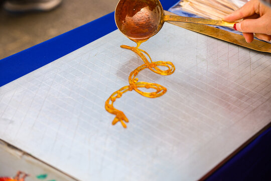 Chinese traditional sugar painting folk craft, artist pouring hot caramel to draw snake pattern on flat board, intangible cultural heritage street art performance