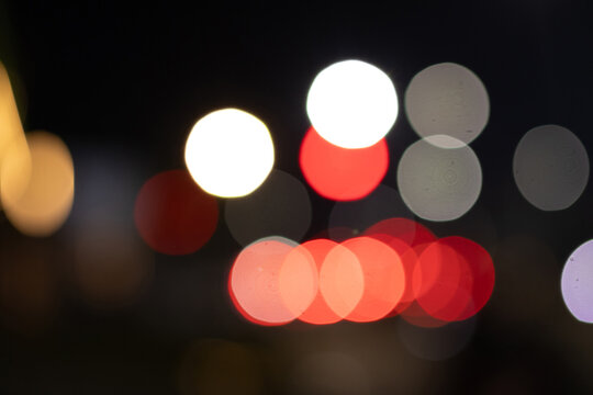 Abstract out of focus night bokeh lights with bright white, red, and subtle warm circles on dark background.