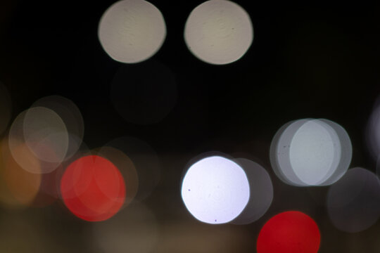Abstract out of focus night bokeh lights with bright white and red circular orbs on dark background.