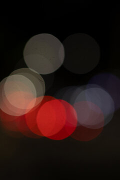 Abstract out of focus colorful night bokeh lights with red, white, and warm orange orbs on dark background.