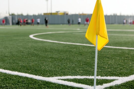 Yellow corner flag on a soccer field with players training in the background