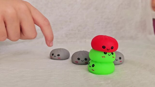 Child hand stacking high tower of colorful kawaii squishy toys and failing as it falls, 4K slow motion clumsy moment
