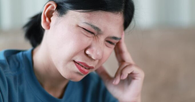 Woman massaging her forehead to relieve headache, migraine, stress, or fatigue, expressing pain, discomfort, health problems, self-care, and wellness, Asian Thai people