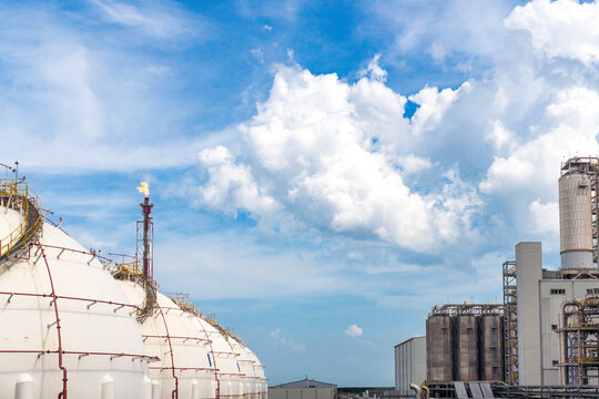 Spherical gas storage tanks and flare stack at a petrochemical plant under a blue sky.