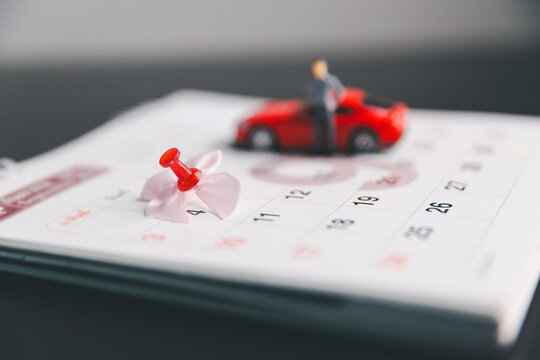 Pushpin marking a calendar date with toy car and driver in background, illustrating vehicle appointment, service schedule, rental booking, payment deadline, insurance renewal and planning.