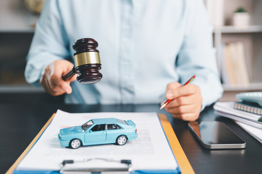 Business professional holding a legal gavel above a car and insurance document, representing auto insurance claims, vehicle law, dispute resolution, accident liability, legal protection