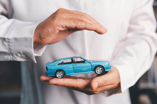 Close-up of hands protecting a blue toy car, symbolizing auto insurance, vehicle safety, accident coverage, warranty, asset protection, ownership security and responsible financial planning.