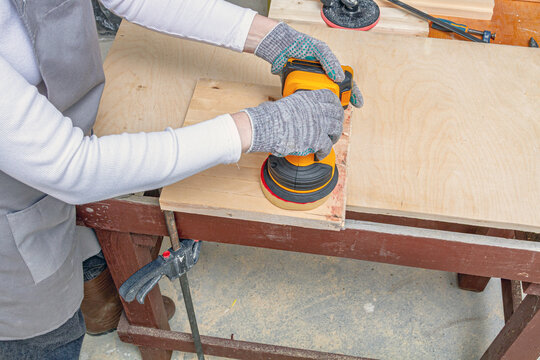 Person sanding a wooden board with an orbital sander at a workbench. Woodworking and surface preparation. DIY repair and furniture making. Carpentry and power tool technique