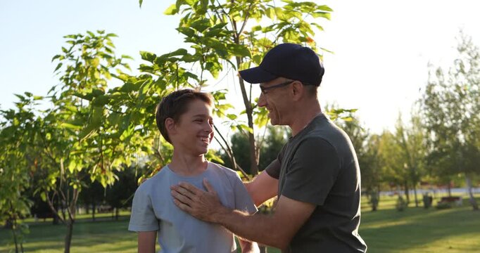 Father and son share family affection as he gives child loving kiss in sunny park. Loving parent and happy child enjoy outdoor quality time. Warm family bonding creates joyful childhood memories.
