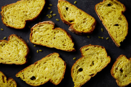 Fresh yellow pumpkin bread with seeds slices. Dark concrete background. Top view.