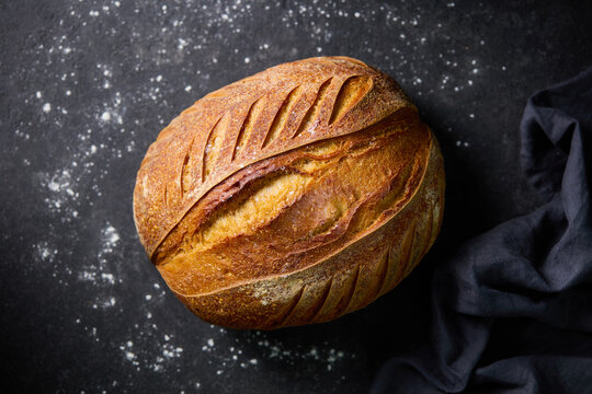 Artisan sourdough bread, tartine loaf. Dark textured stone background. Close up. Top view.