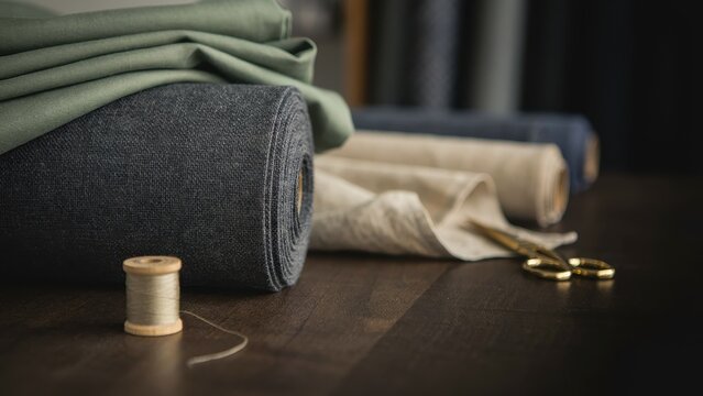 Rolled fabrics and sewing supplies on a wooden table, textile industry concept.