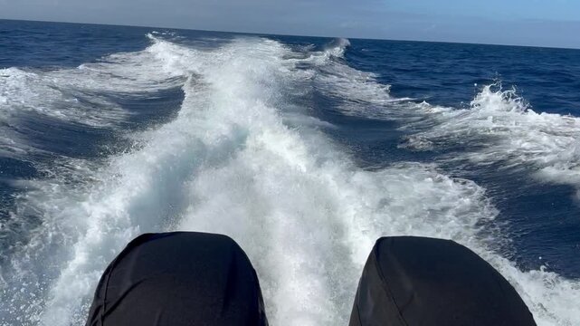 Powerful motorboat speeding across the open sea, leaving a dramatic foamy wake behind as twin outboard engines propel the vessel through deep blue water.