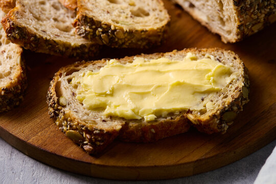 Fresh multi seed artisanal sourdough bread with butter spread on a board. Close up.