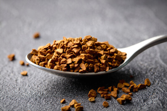 Aromatic instant freeze-dried coffee granules in a metal spoon. Grey stone background. Close up.