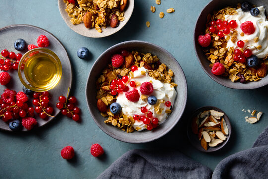 Healthy breakfast bowls with granola yogurt and fresh berries on teal background. Top view.