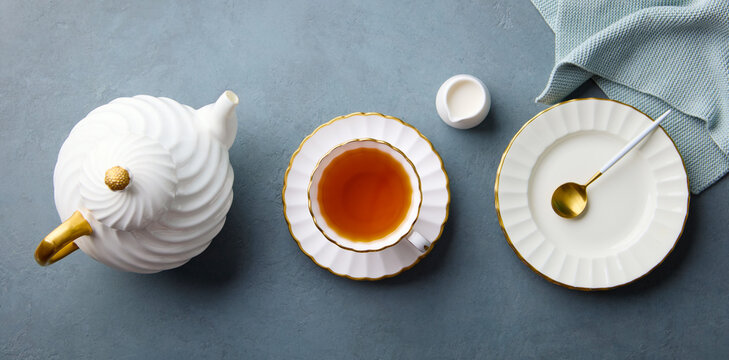 Traditional English afternoon tea setting with ceramic tableware, creamer and spoon. Grey blue stone background. Top view.