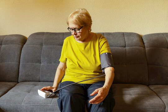 Senior woman measuring blood pressure at home on sofa