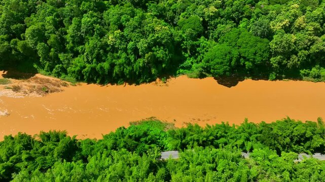 Aerial view captures a flooded tropical river winding through lush forest, emphasizing high water levels, sediment runoff, ecosystem resilience, and natural flood cycles. Phrae Province, Thailand. 4k.