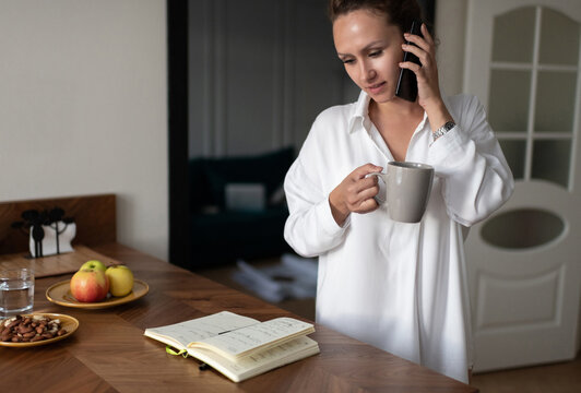 Businesswoman with mug answering phone call at home