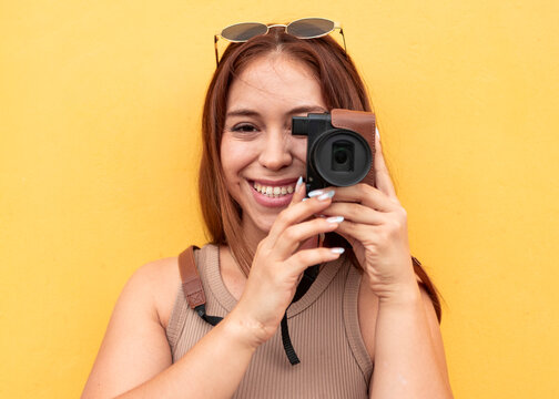 Smiling woman use instant camera against yellow background