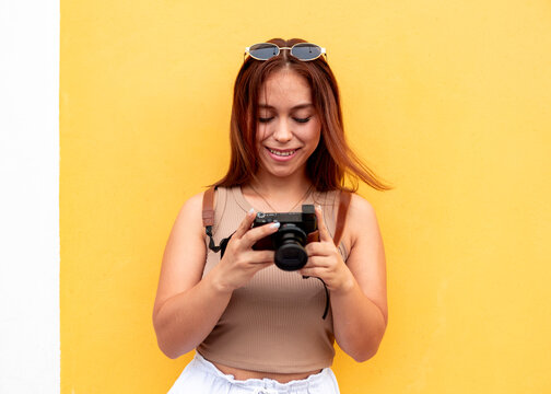 Smiling woman review camera photo against yellow wall