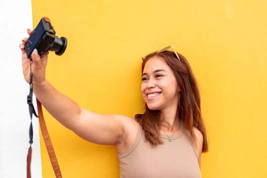 Smiling woman take selfie with camera against yellow wall