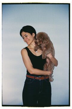 Woman holds poodle dog while smiling in a simple indoor setting