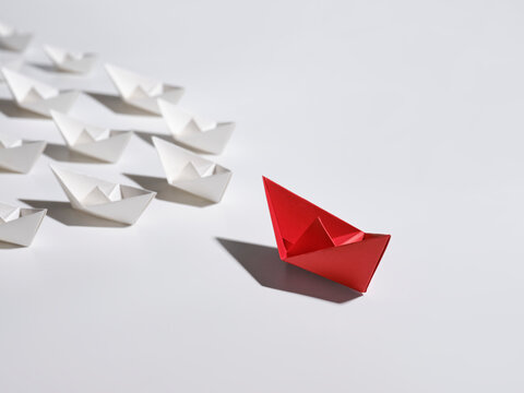Red origami boat leads a fleet of white paper boats
